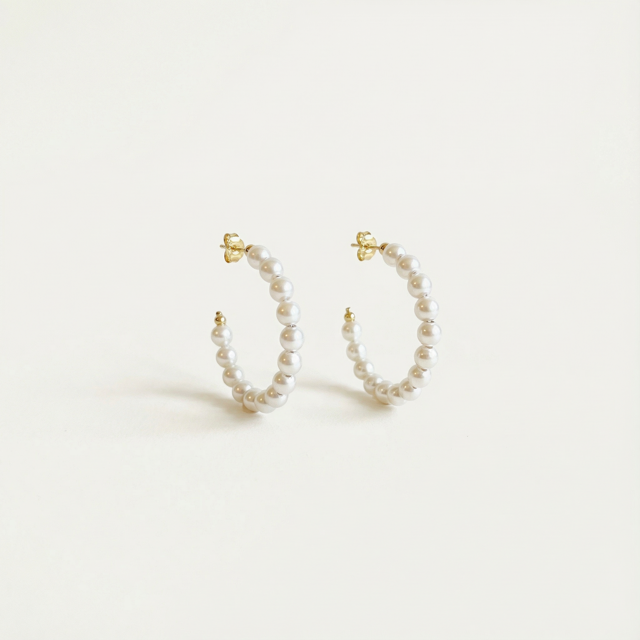 Pair of pearl hoop earrings on a light beige background