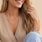 Woman wearing a beige sweater and gold jewelry on a neutral background