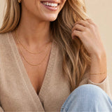 Woman wearing a beige sweater and gold jewelry on a neutral background