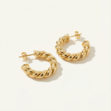 18k gold hoops for women laying down on a beige background