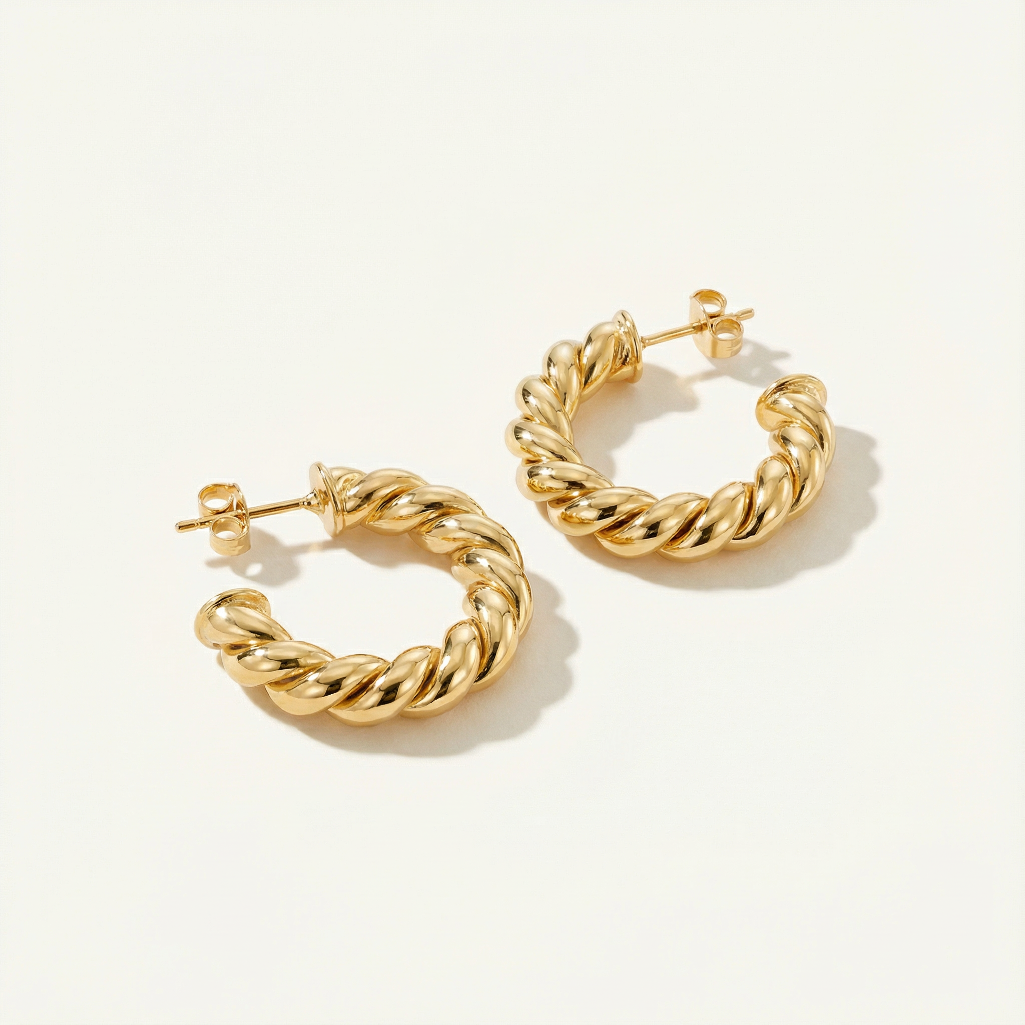 18k gold hoops for women laying down on a beige background