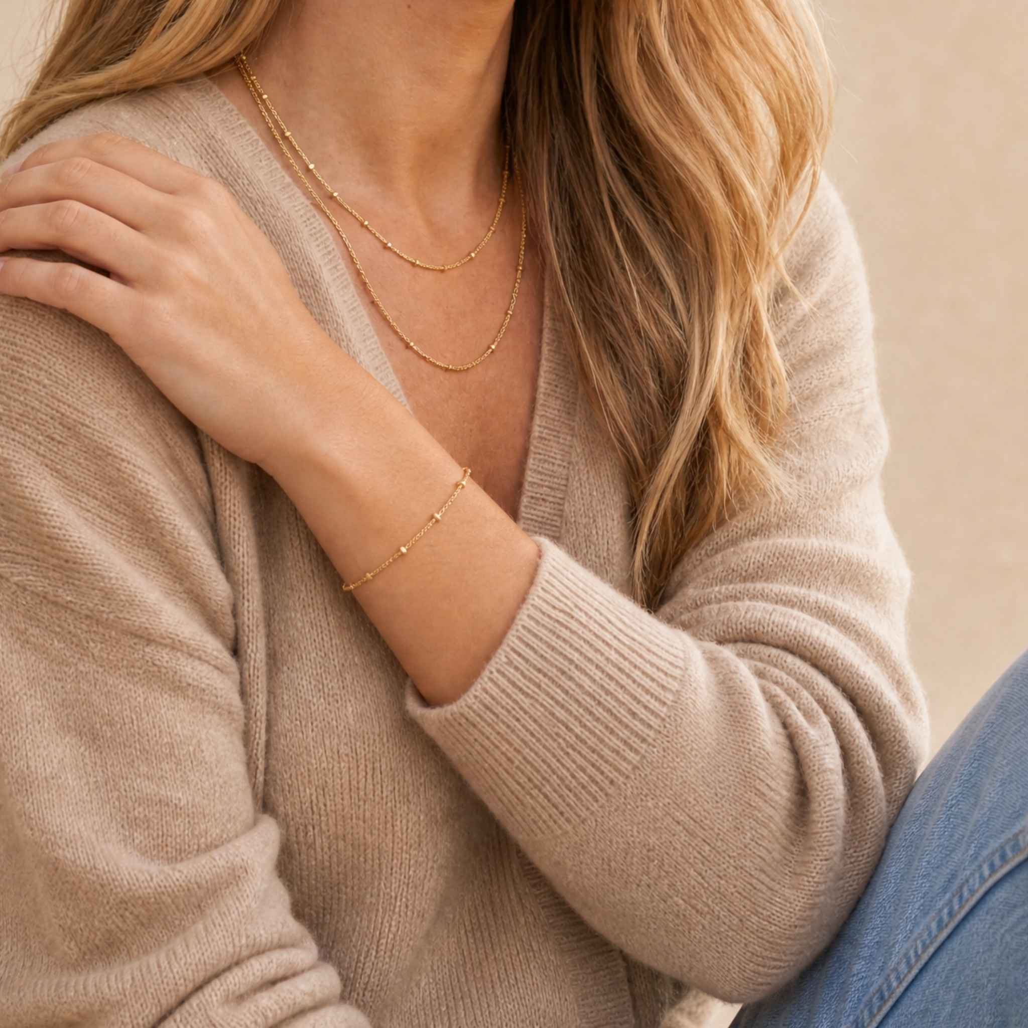 Person wearing a beige sweater and gold tarnish free bracelet with a neutral background