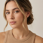 Woman wearing gold heart stud earrings against a neutral background
