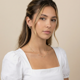 Woman wearing a delicate necklace and gold hoop earrings against a beige background
