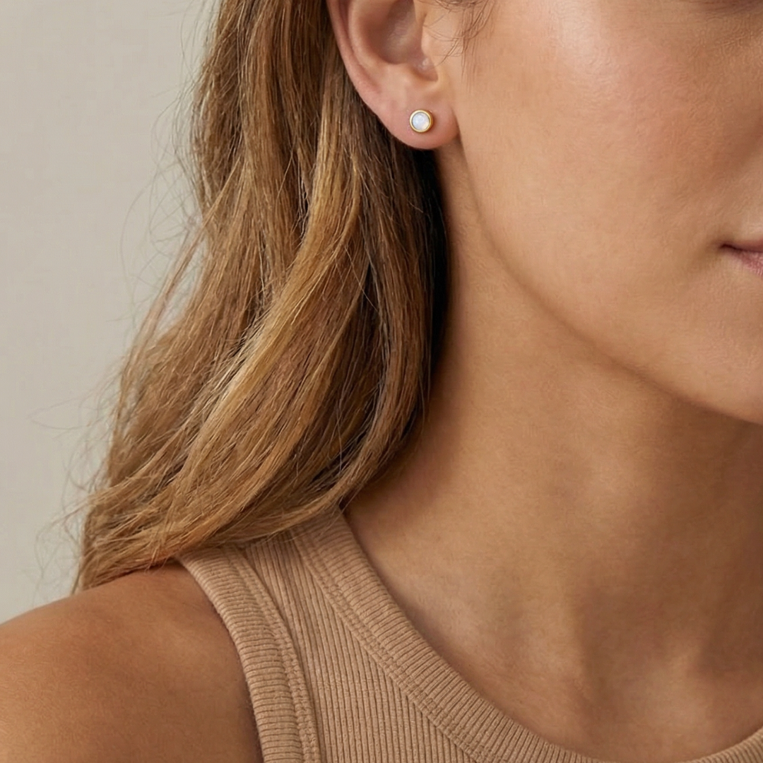Close-up of a person wearing an opal stud earring with a neutral background