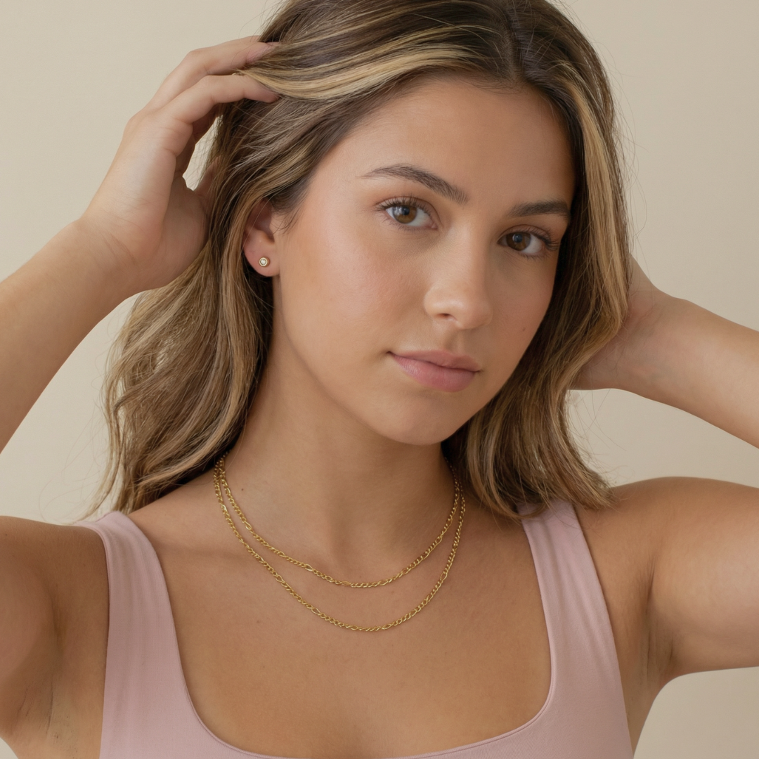 Woman wearing gold figaro necklaces against a neutral background