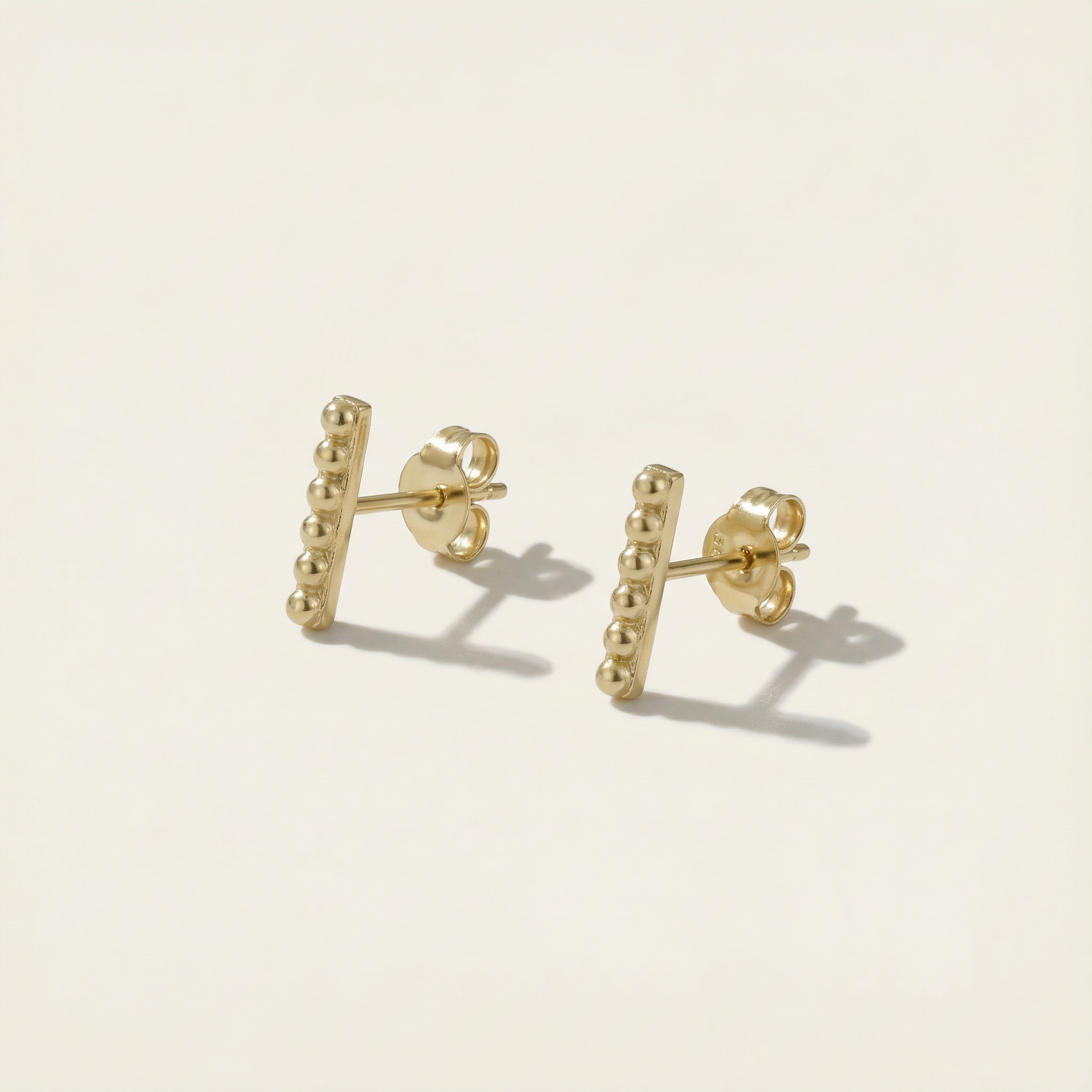 Gold bar stud earrings on a light beige background
