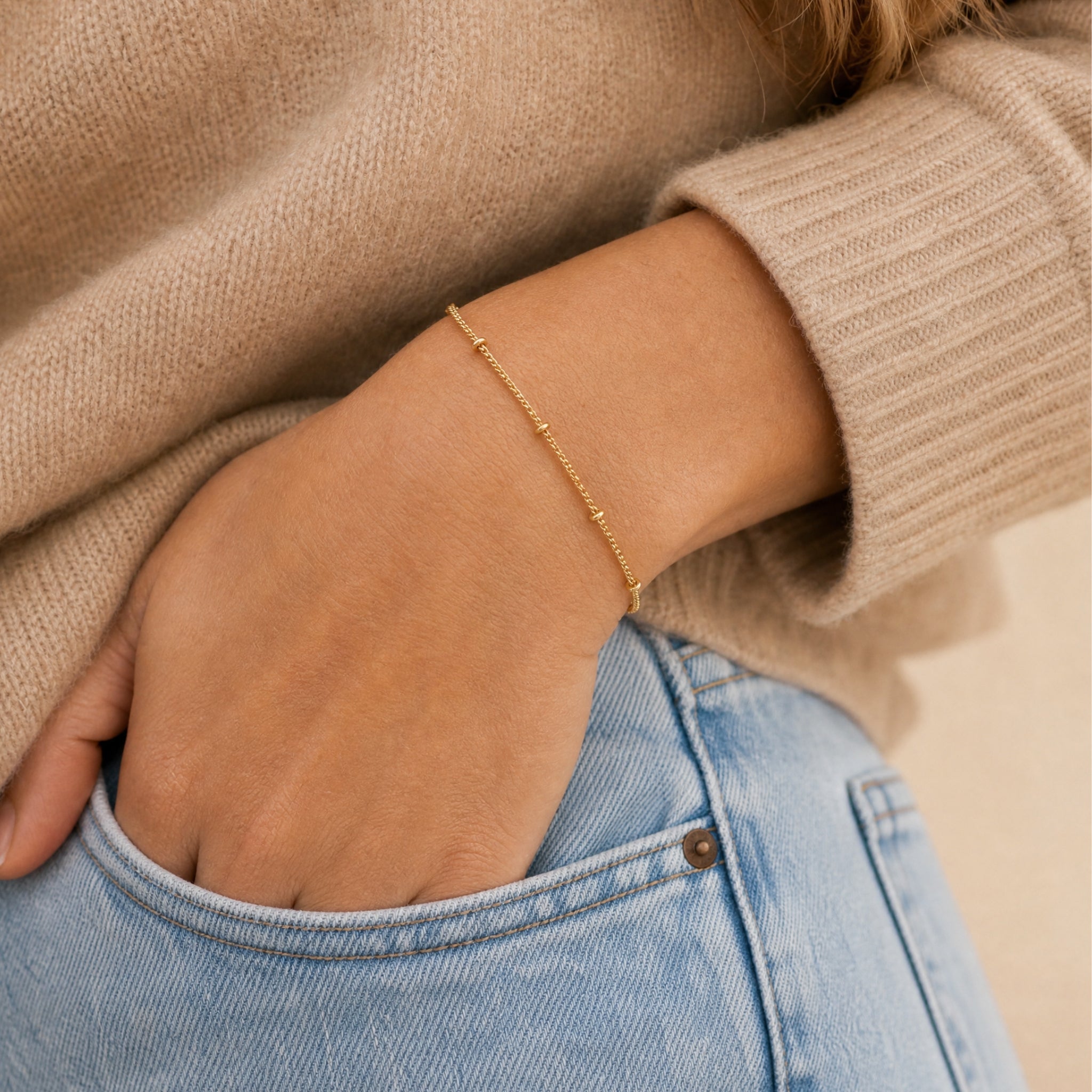 Gold bracelet on a wrist with a neutral background