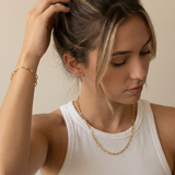 Woman wearing a gold necklace and bracelet against a neutral background