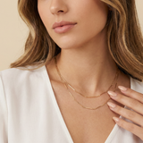 Close-up of a woman wearing a gold dainty necklace against a beige background