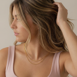 Woman wearing a gold figaro necklace with a neutral background