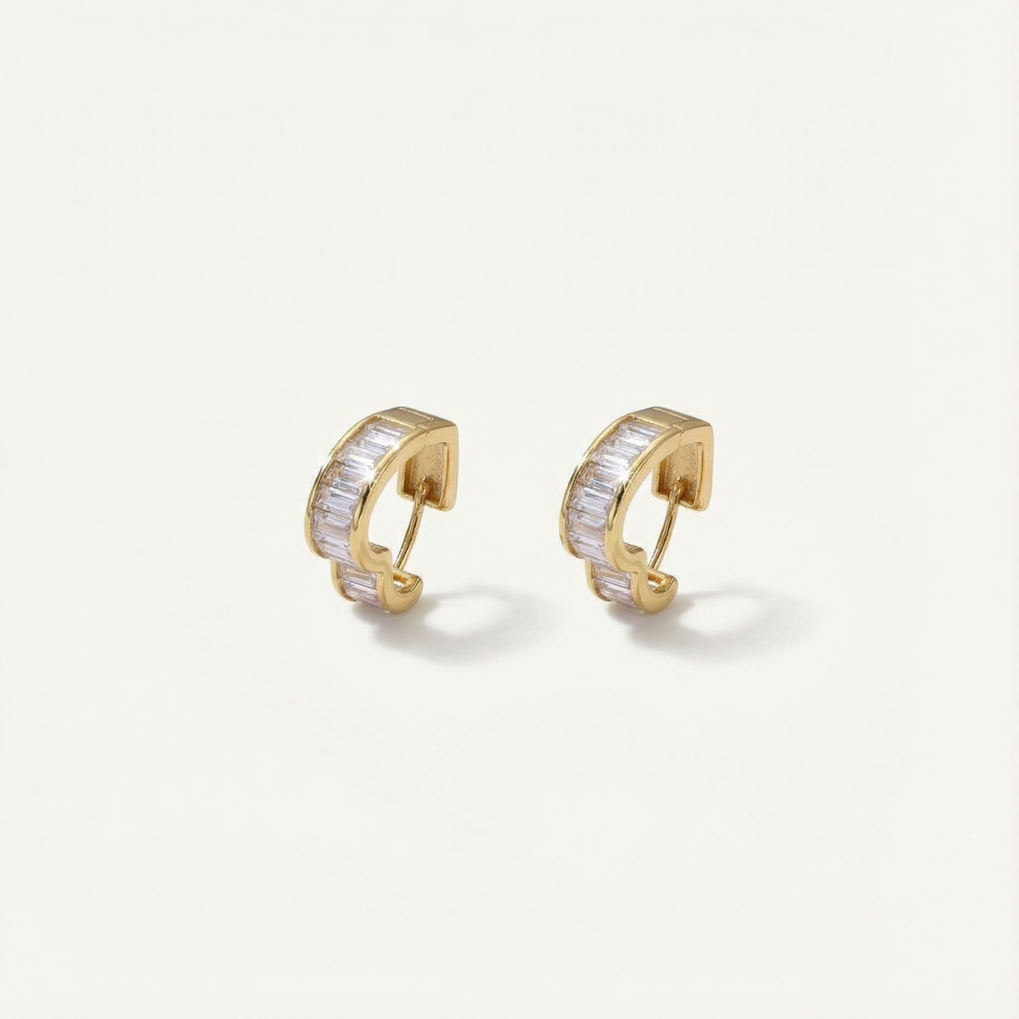 Gold hoop earrings with clear stones on a light beige background