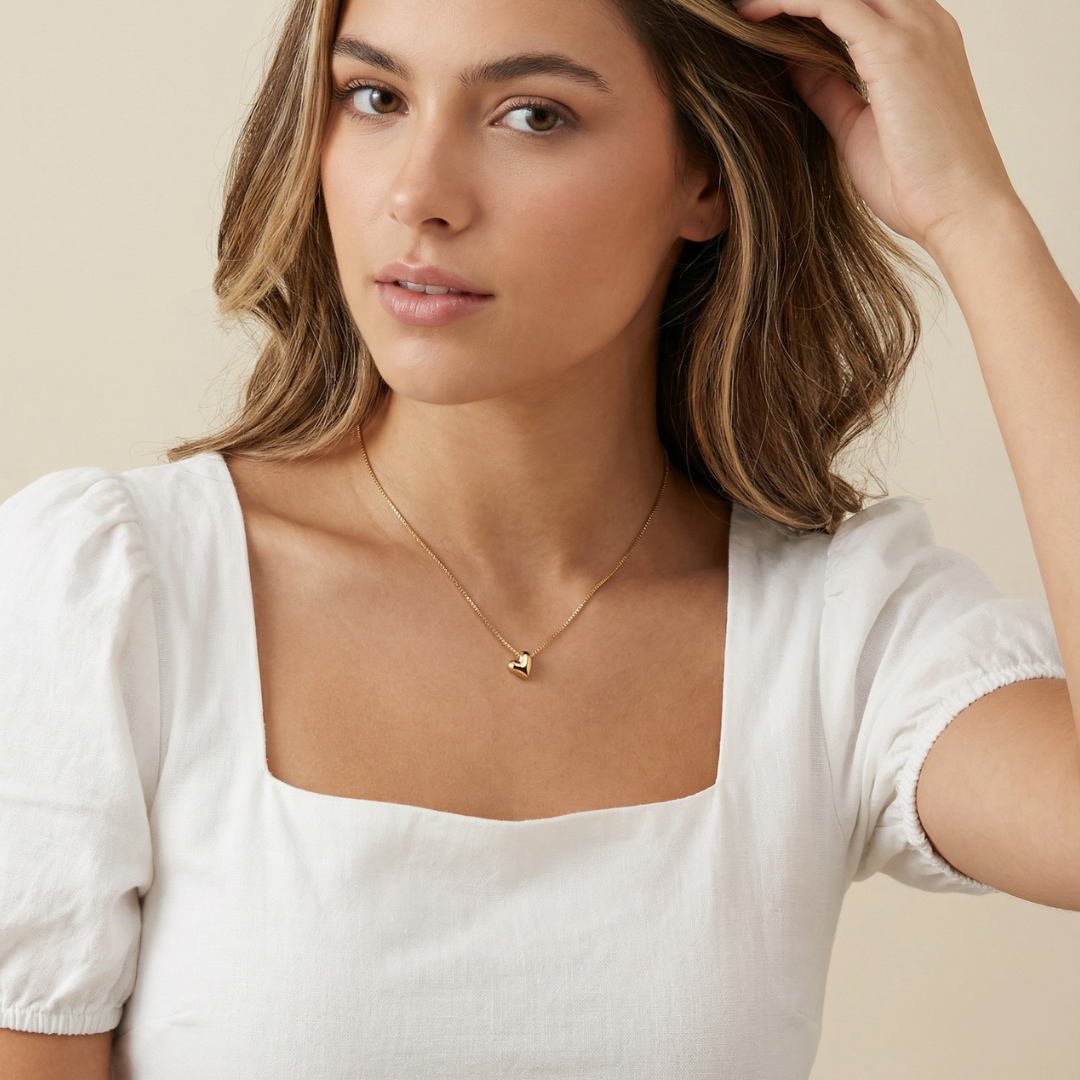 Woman wearing a gold heart necklace against a beige background