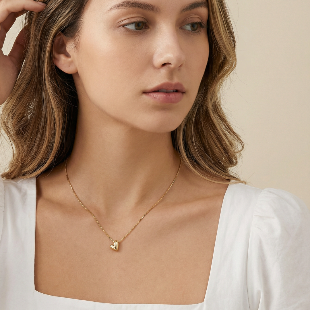 Woman wearing a gold heart pendant necklace against a beige background