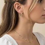 Close-up of a woman wearing gold hoops and necklace against a neutral background