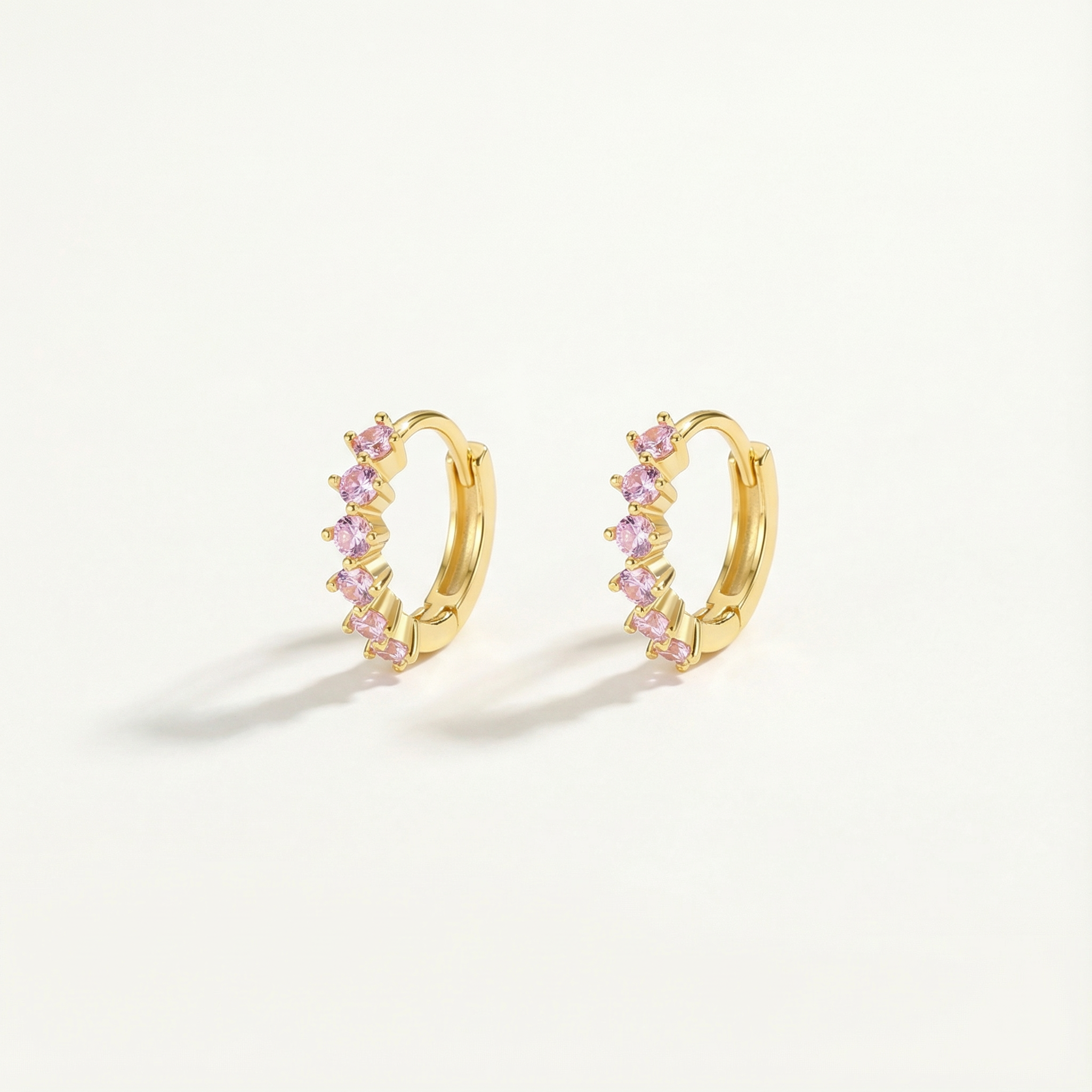 Gold hoop earrings with pink gemstones on a light beige background