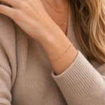 Gold dainty bracelet on a person wearing a beige sweater