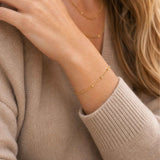 Gold dainty bracelet on a person wearing a beige sweater