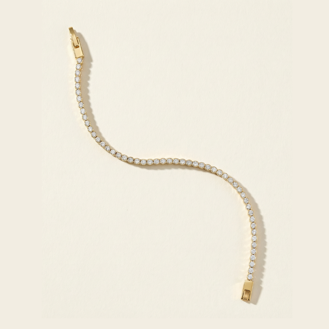 Gold tennis bracelet with clear cubic zirconia stones on a beige background