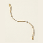 Gold tennis bracelet with clear cubic zirconia stones on a beige background