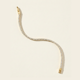 Gold tennis bracelet with clear cubic zirconia stones on a beige background