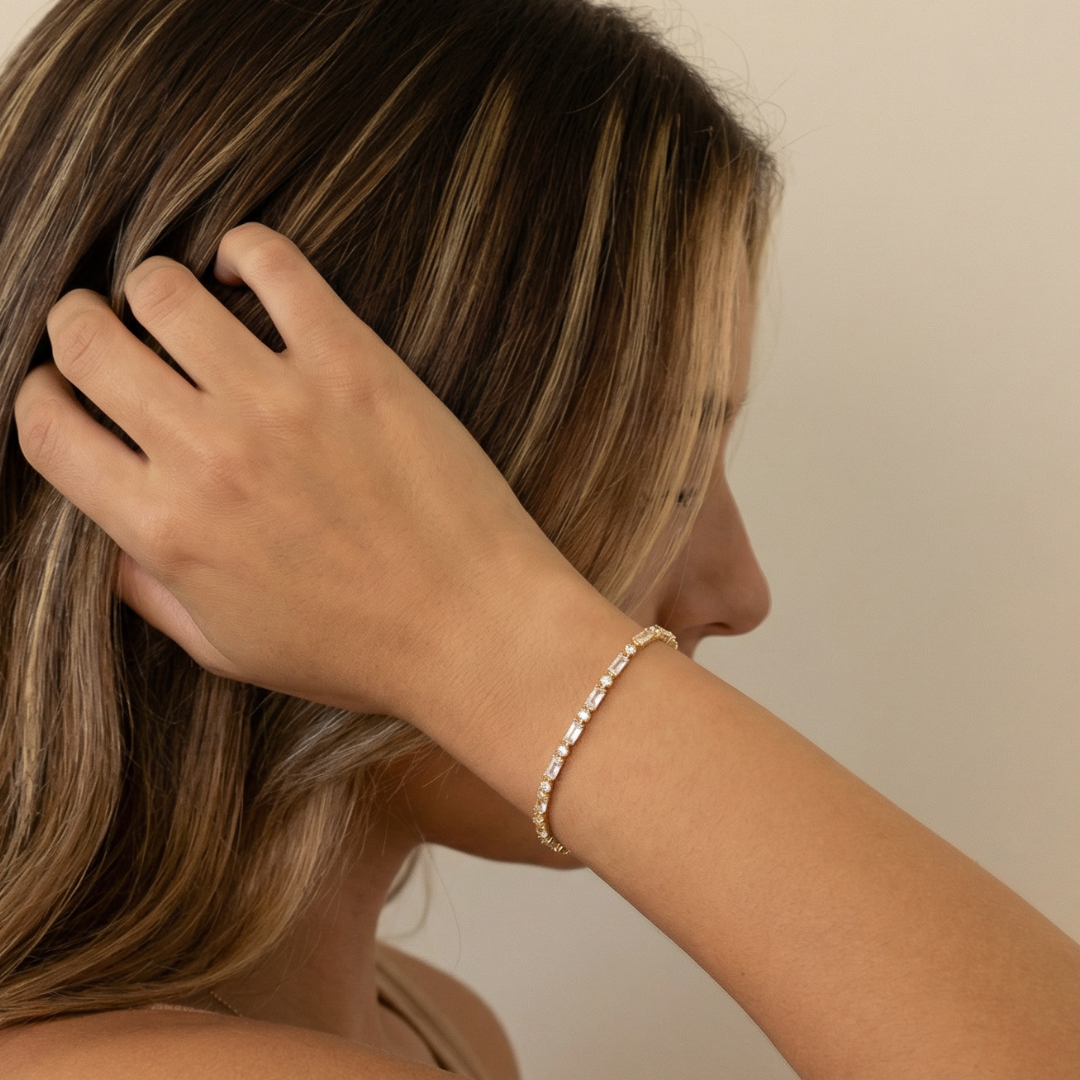 Women with hand in hair wearing a gold bracelet on a neutral background