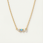 Gold necklace with three gemstones on a light beige background