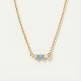 Gold necklace with three gemstones on a light beige background