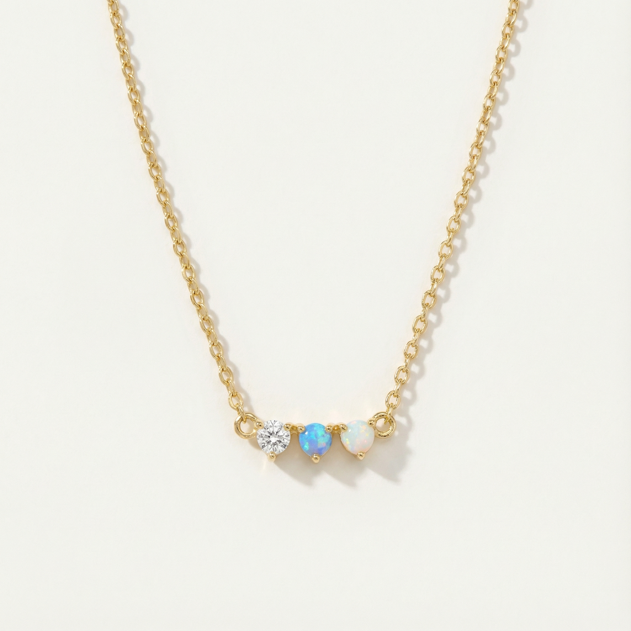 Gold necklace with three gemstones on a light beige background