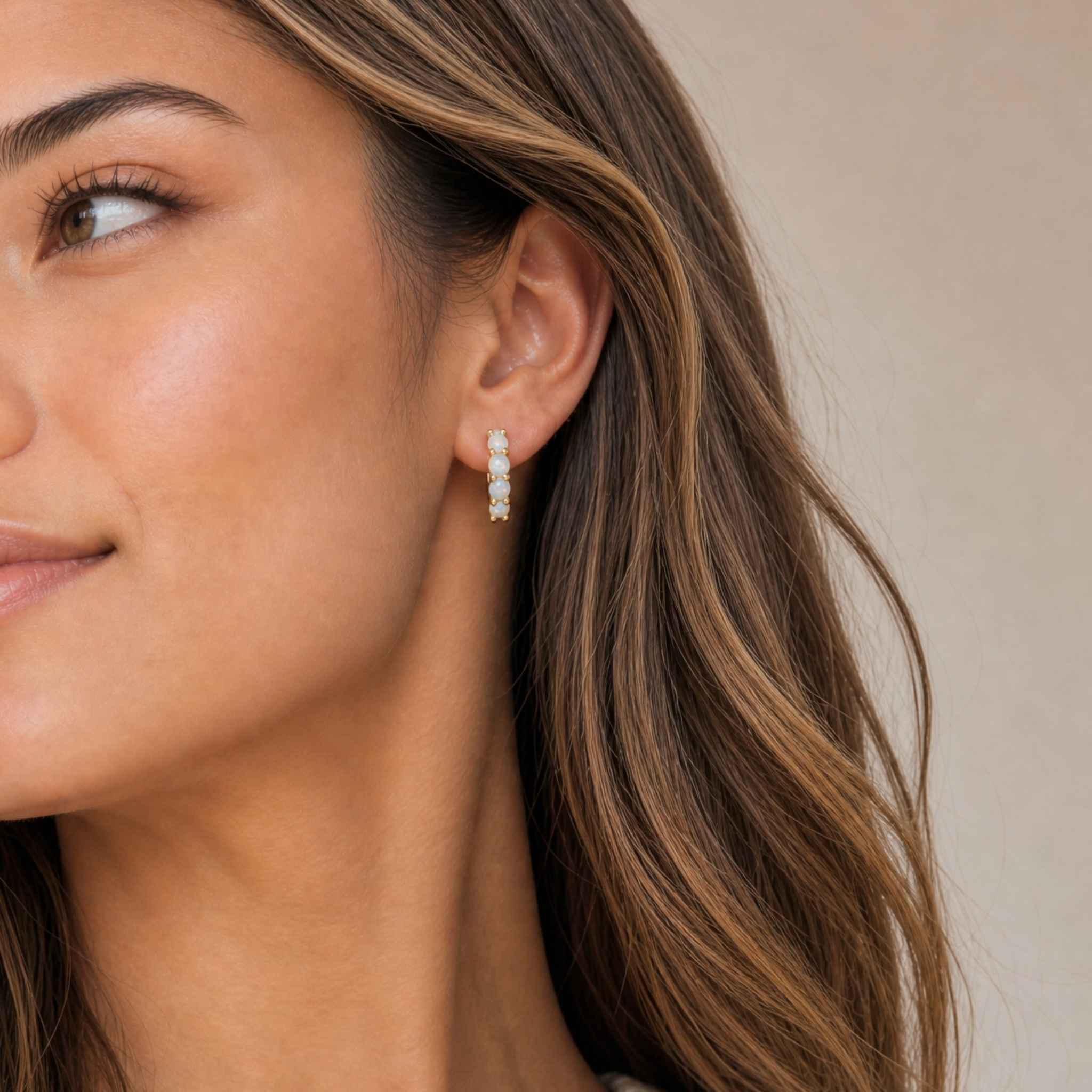 Close-up of a woman wearing hypoallergenic opal earrings with a neutral background