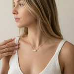 Woman wearing a dainty opal necklace with a minimalistic pendant against a neutral background