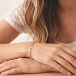 Woman resting her crossed hands on a table wearing the Figaro Bracelet, a dainty stackable gold chain bracelet by Kate Gates Jewelry