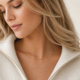 A close-up lifestyle shot of a woman wearing a hypoallergenic gold chain necklace and a cream-colored ribbed zip-up sweater.