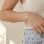 Person wearing a gold herringbone bracelet on a neutral background
