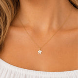 model wearing gold necklace with white enamel daisy flower pendant