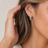 Close-up of a person wearing gold hoop earrings with a neutral background